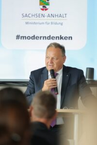 Man in a suit speaks into a microphone at a lectern, with a banner reading Sachsen-Anhalt Ministerium für Bildung and #moderndenken.